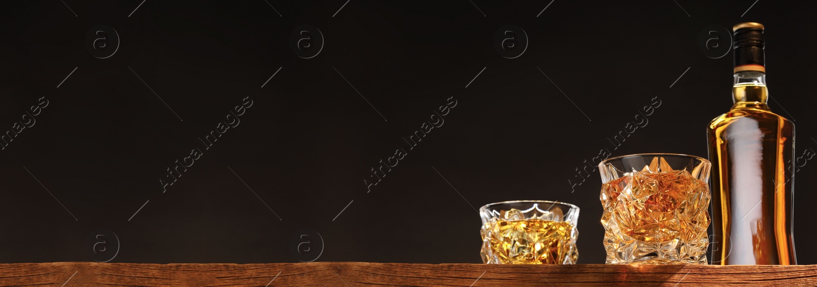 Image of Whiskey in glasses and bottle on wooden table, low angle view. Banner design with space for text