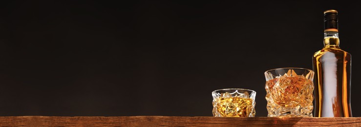 Whiskey in glasses and bottle on wooden table, low angle view. Banner design with space for text