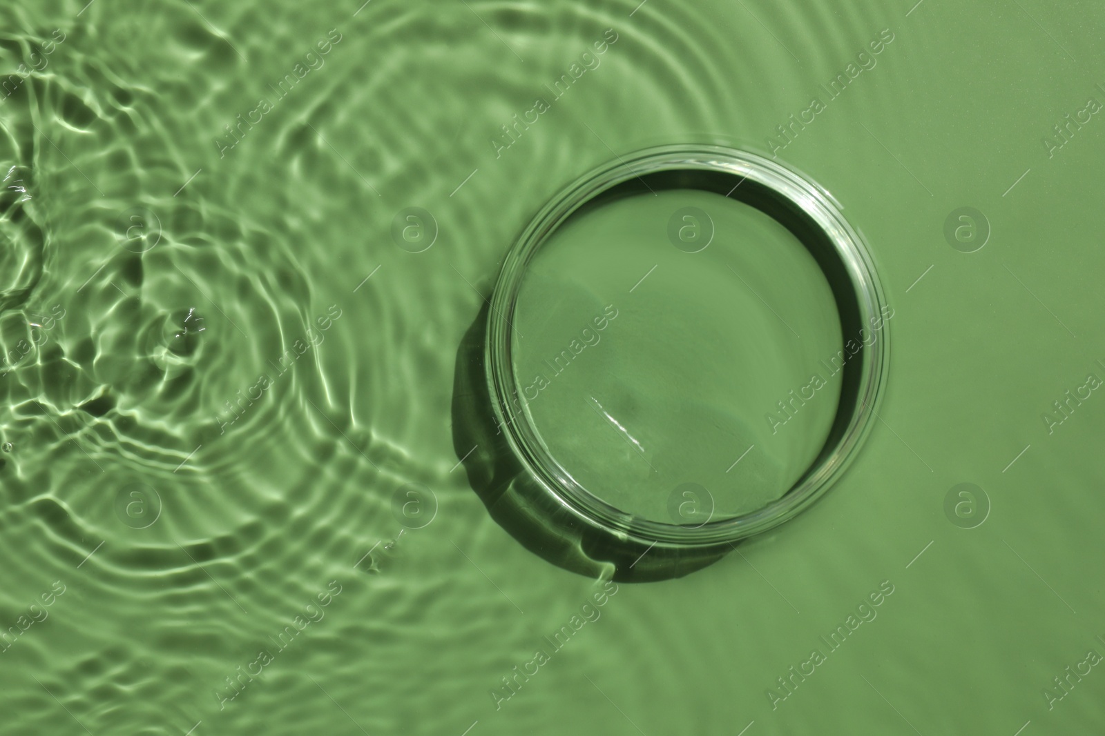 Photo of Stylish presentation for product. Glass podium in water on pale green background, top view