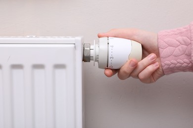 Photo of Girl adjusting heating radiator thermostat near white wall indoors, closeup