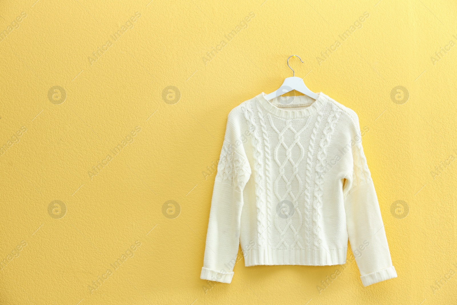 Photo of Hanger with stylish sweater on yellow wall. Space for text