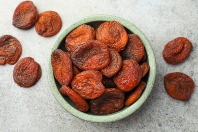 Photo of Bowl with tasty apricots on grey table, flat lay. Dried fruits