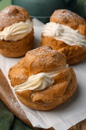 Photo of Delicious profiteroles filled with cream on green fabric, closeup