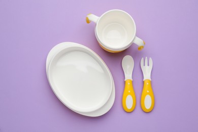 Set of plastic dishware on violet background, flat lay. Serving baby food