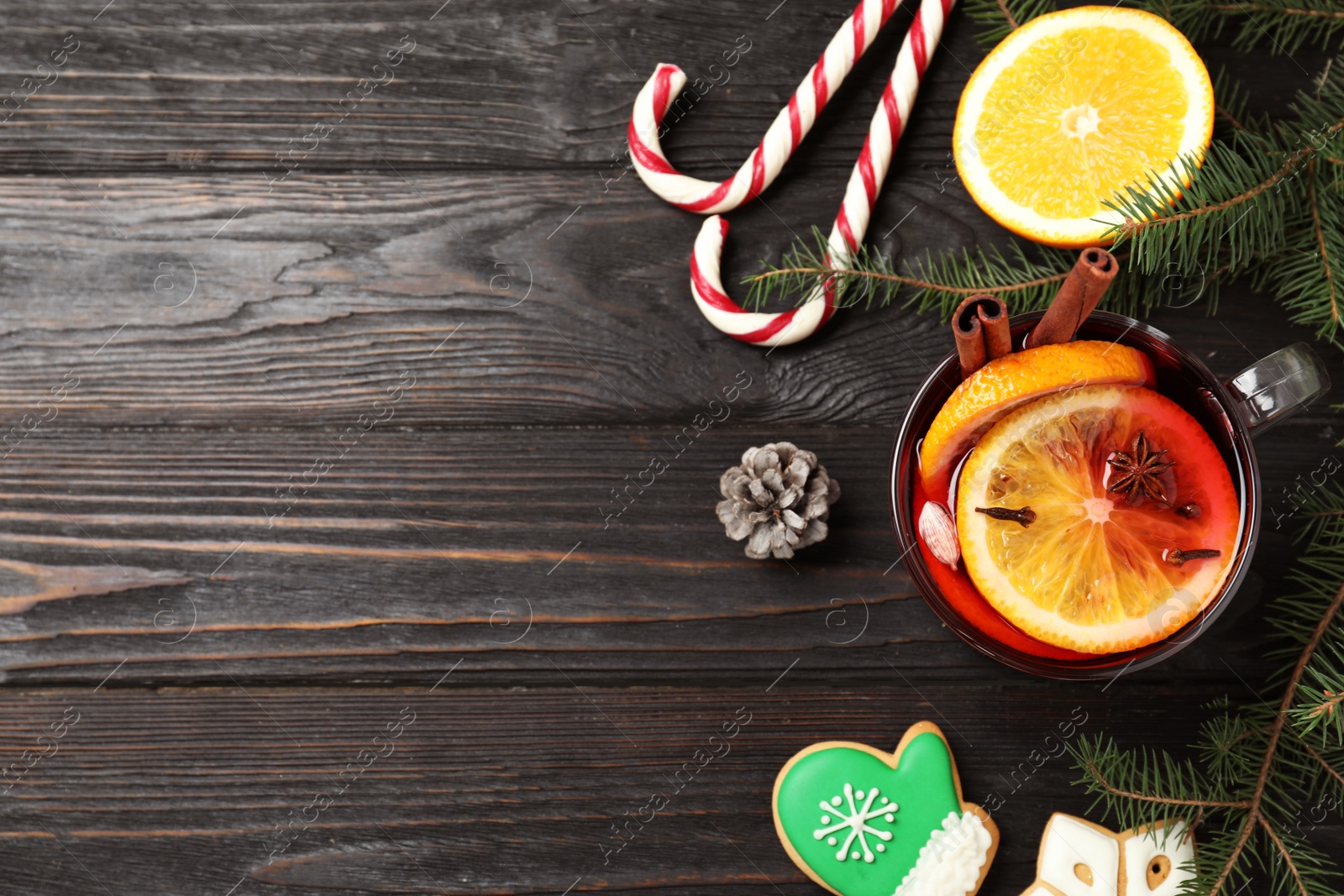 Photo of Glass cup of tasty mulled wine on black wooden table, flat lay. Space for text