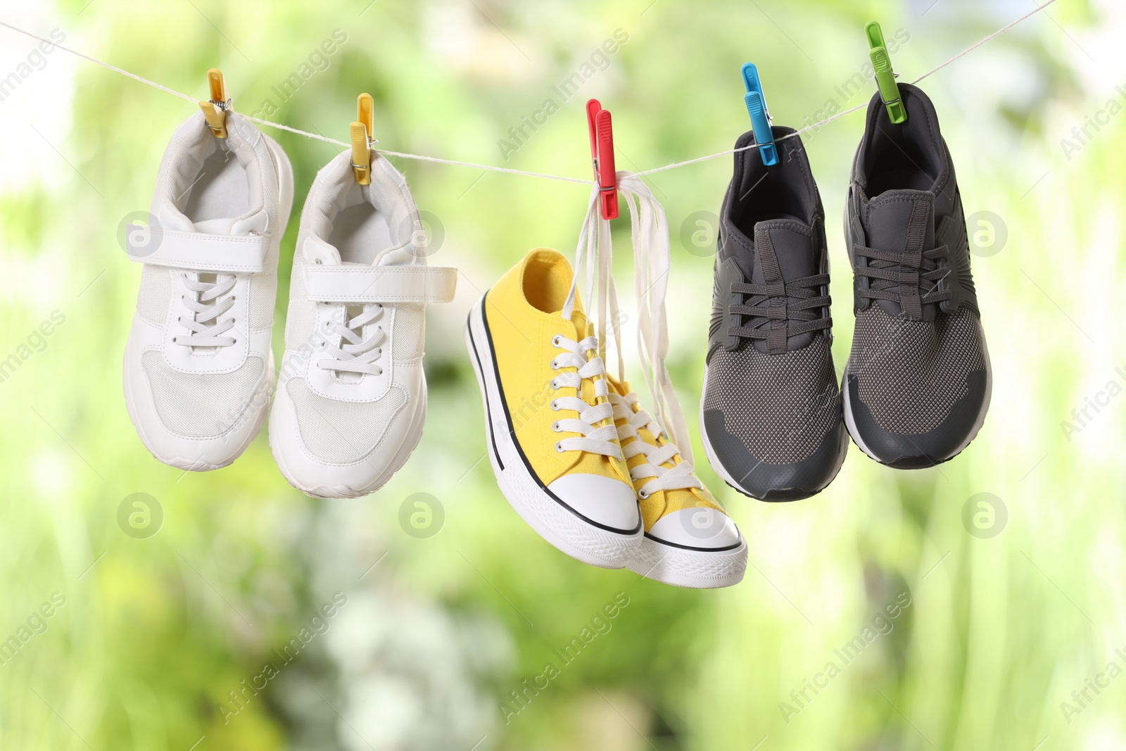 Photo of Different stylish sneakers drying on washing line against blurred background