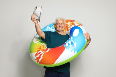 Funny mature man with bright inflatable ring on light background