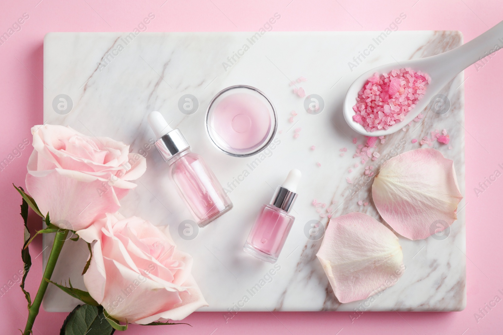 Photo of Stone board with rose essential oil, salt and flowers on pink background