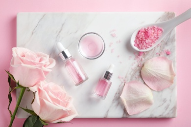 Stone board with rose essential oil, salt and flowers on pink background