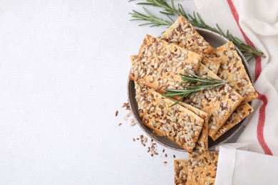 Photo of Cereal crackers with flax, sunflower, sesame seeds and rosemary in bowl on white table, top view. Space for text