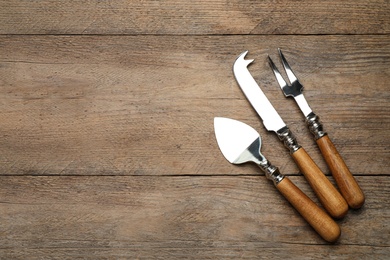 Photo of Cheese knives and fork on wooden table, flat lay. Space for text