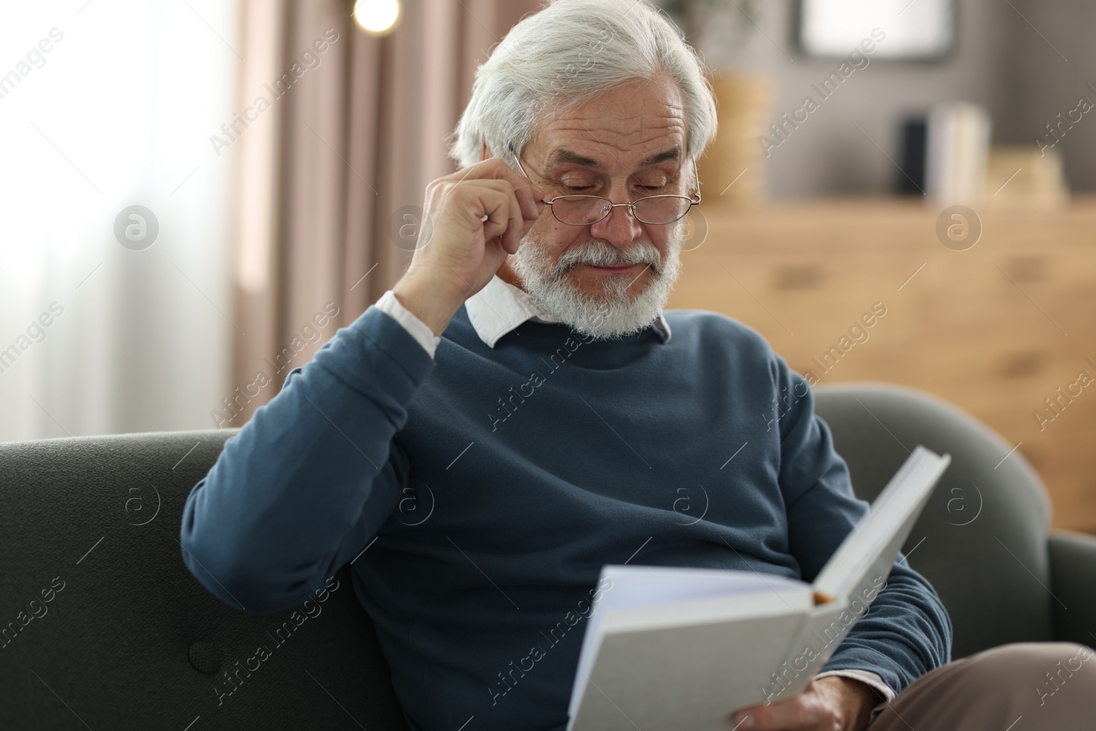 Photo of Portrait of happy grandpa reading book on sofa indoors