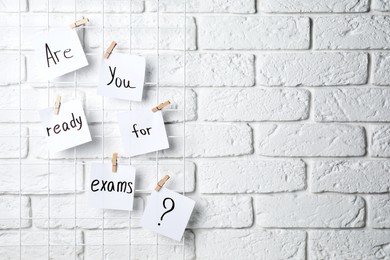 Photo of Notes with phrase Are you ready for exams hanging on white brick wall, space for text