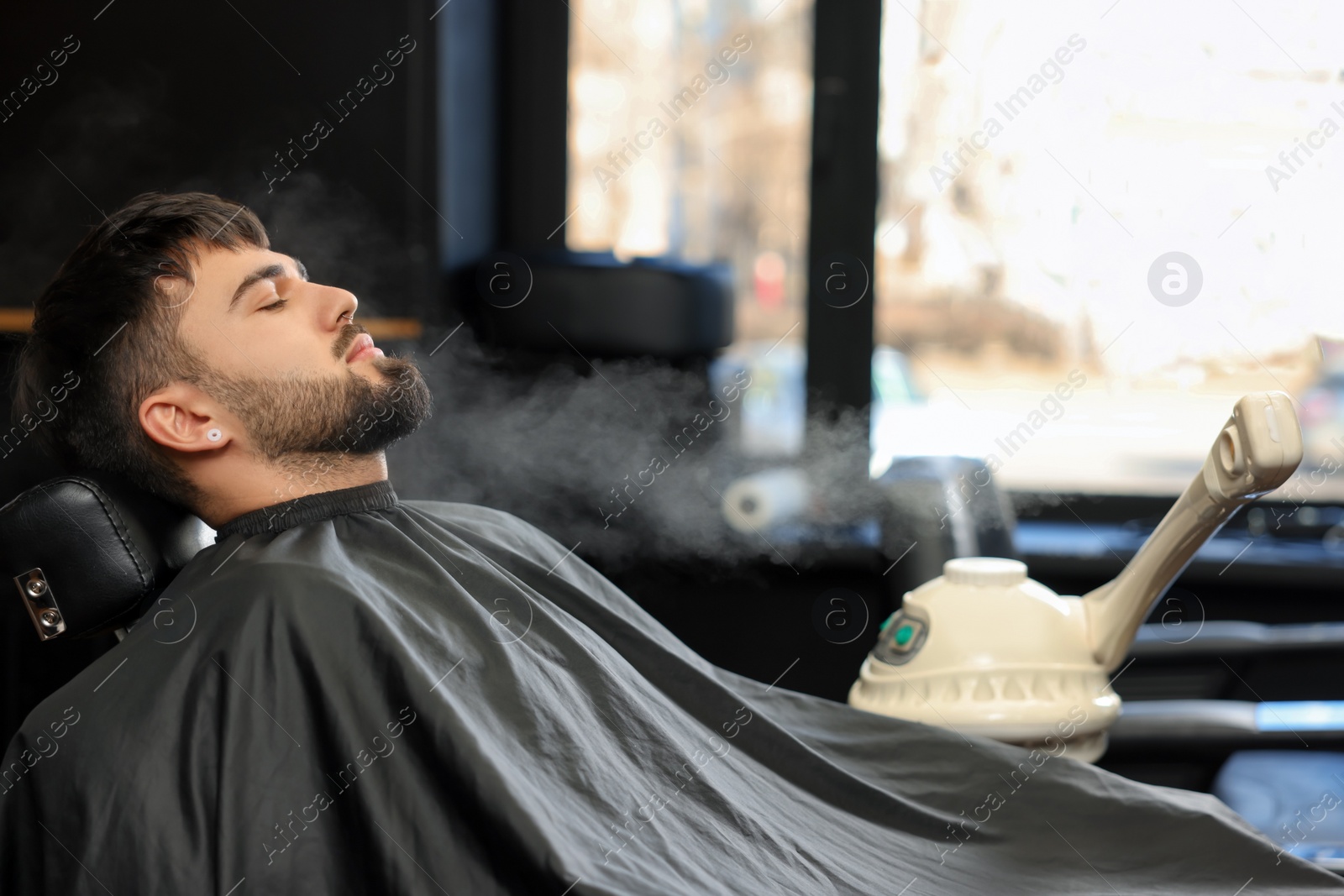 Photo of Young bearded man visiting barbershop. Professional shaving service