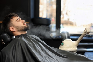 Photo of Young bearded man visiting barbershop. Professional shaving service