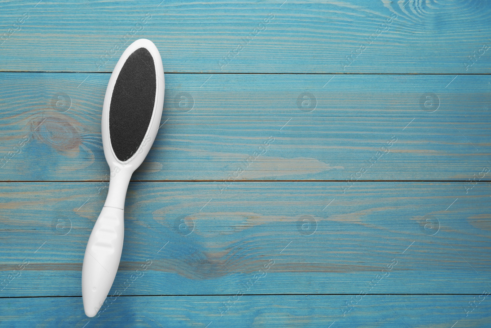 Photo of White foot file on light blue wooden table, top view with space for text. Pedicure tool