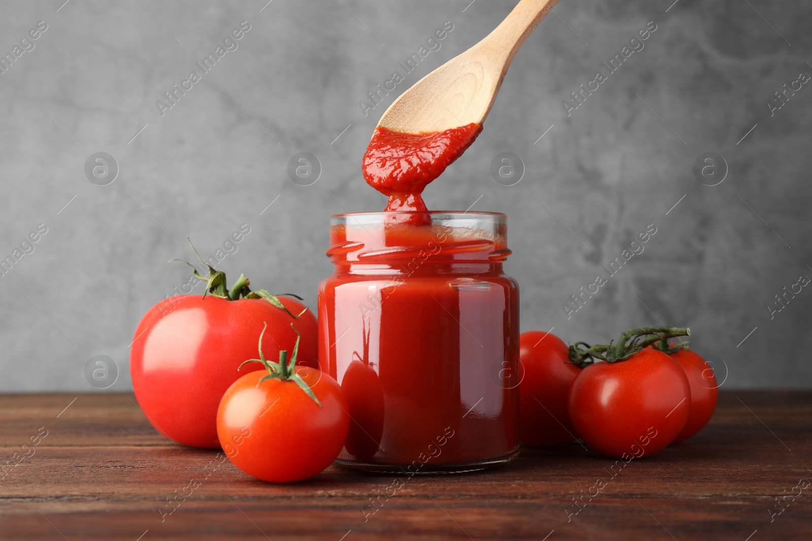 Photo of Taking tasty ketchup with spoon from jar on wooden table, closeup