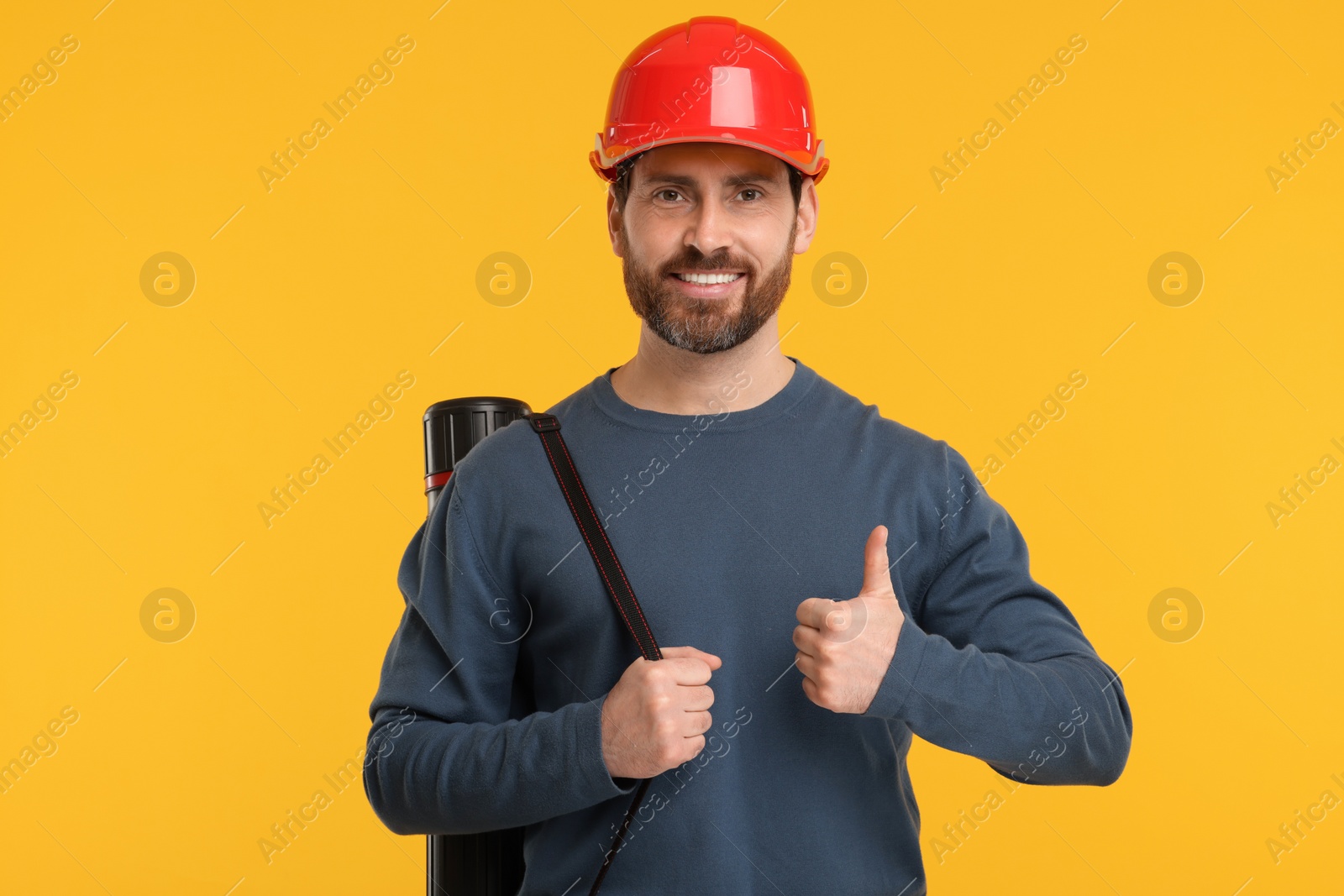 Photo of Architect in hard hat with drawing tube showing thumbs up on orange background