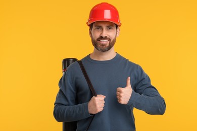 Architect in hard hat with drawing tube showing thumbs up on orange background