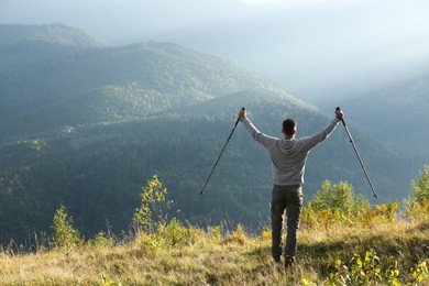 Man with trekking poles hiking in mountains, back view. Space for text