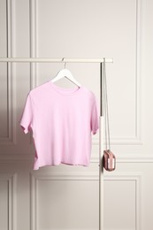 Rack with stylish pink t-shirt and shiny bag near white wall