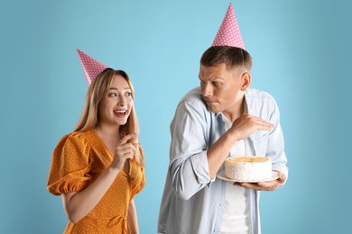 Photo of Greedy man hiding birthday cake from woman on turquoise background