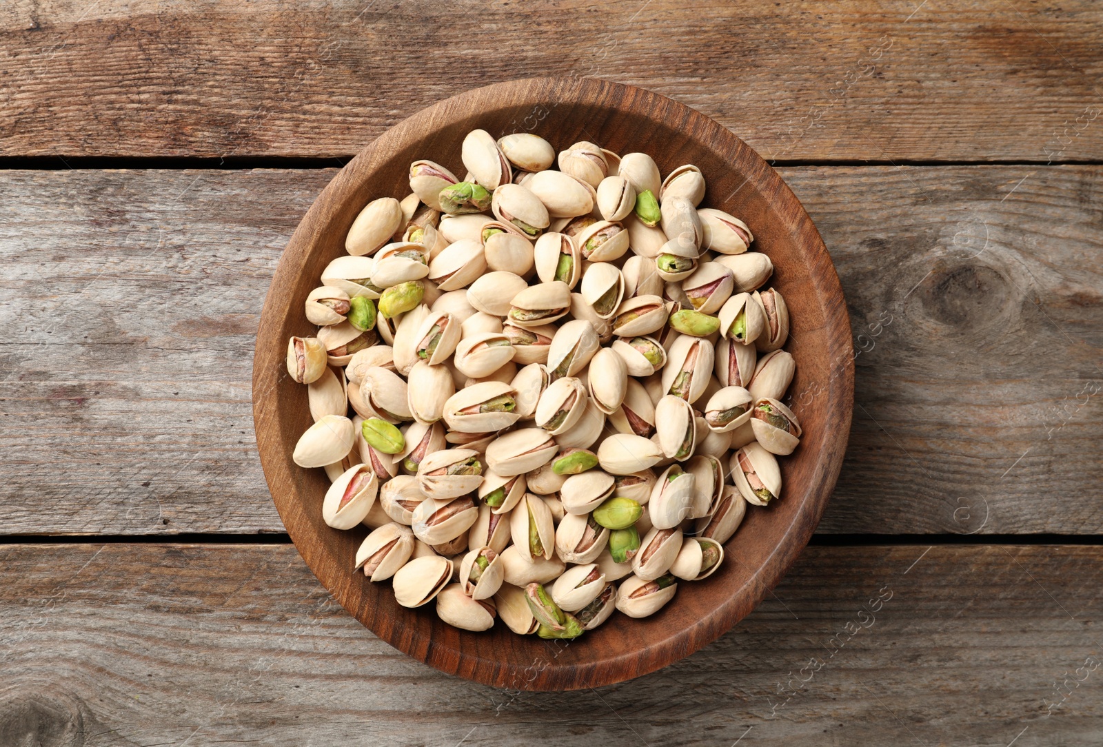 Photo of Organic pistachio nuts in bowl on wooden table, top view