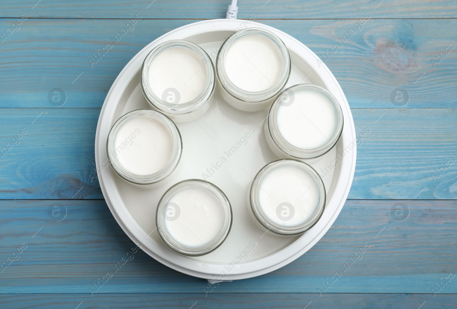 Photo of Modern yogurt maker with full jars on blue wooden table, flat lay