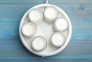 Modern yogurt maker with full jars on blue wooden table, flat lay
