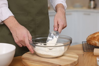 Making bread. Man putting flour into bowl at wooden table in kitchen, closeup