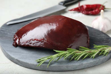 Photo of Piece of raw beef liver with rosemary on light table, closeup
