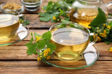 Photo of Glass cup of aromatic celandine tea and flowers on wooden table