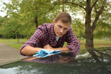 Man washing car hood with rag outdoors