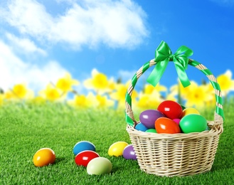 Image of Wicker basket with Easter eggs on green grass outdoors, space for text