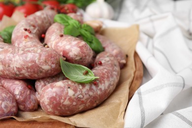Photo of Raw homemade sausages, basil leaves and peppercorns on table, closeup