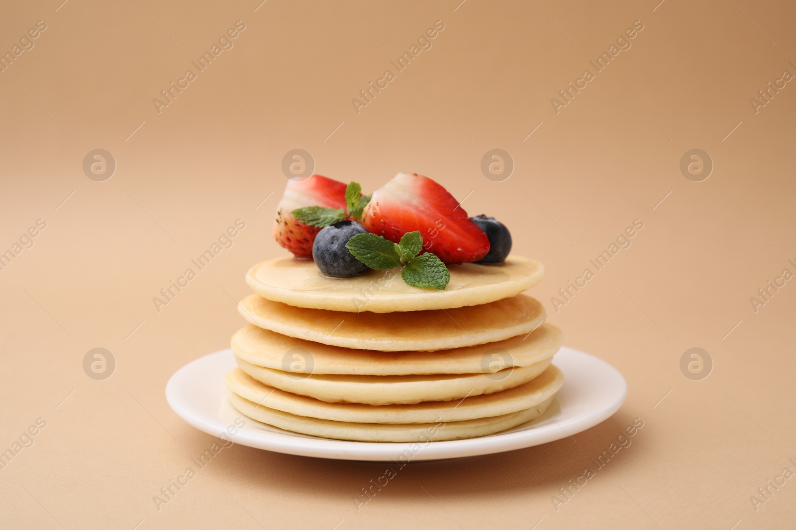 Photo of Stack of tasty pancakes with fresh berries and mint on beige background