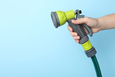 Photo of Woman holding watering hose with sprinkler on light blue background, closeup. Space for text