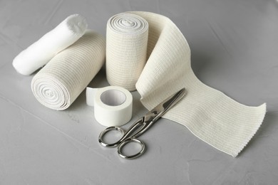 Photo of Medical bandage rolls, sticking plaster and scissors on grey table