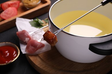 Photo of Fondue pot, forks with meat pieces and other products on black textured table, closeup