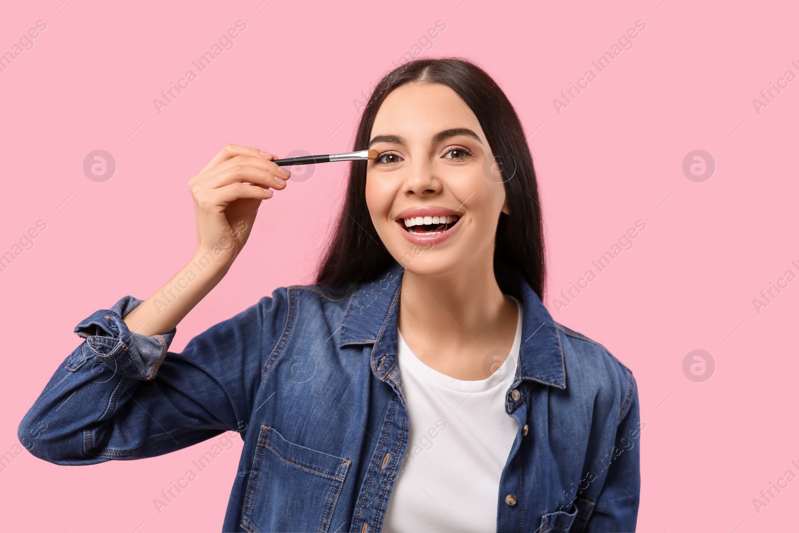 Photo of Beautiful woman applying makeup with brush on pink background