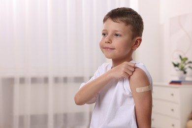 Photo of Boy with sticking plaster on arm after vaccination indoors, space for text