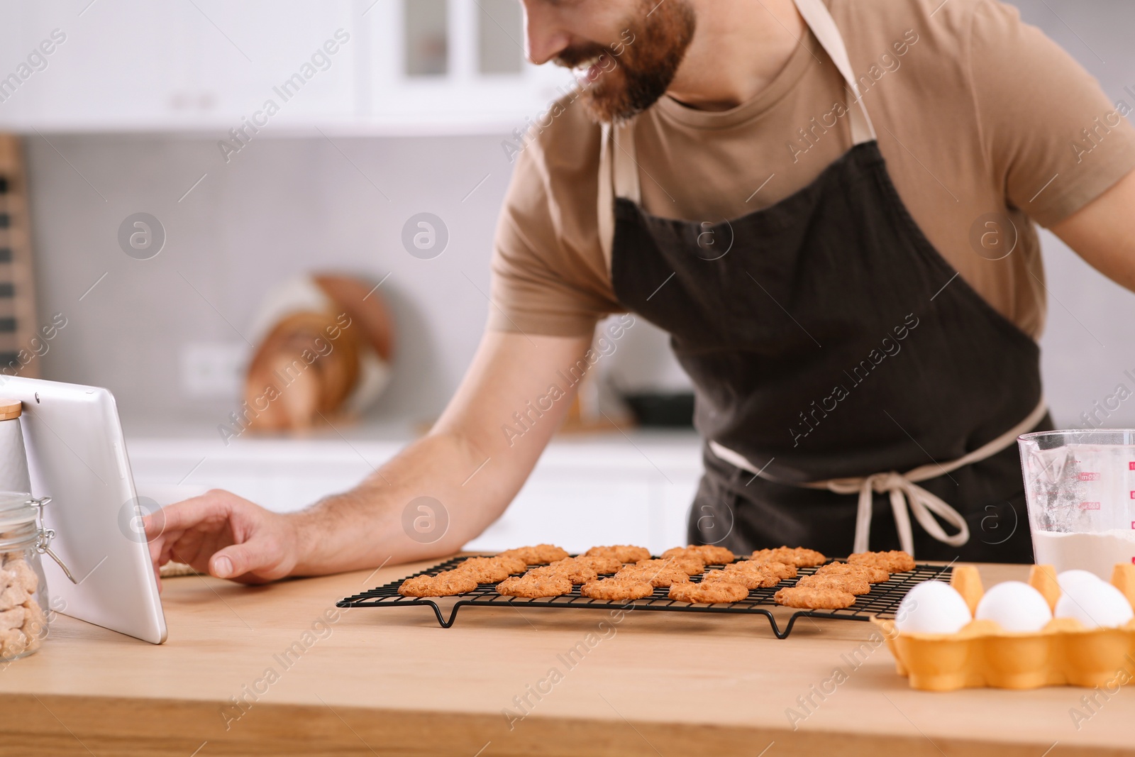 Photo of Man with freshly baked cookies watching online cooking course via tablet in kitchen, closeup