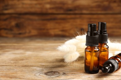Photo of Bottles with oil and fluffy wildflowers on wooden table, space for text. Natural cosmetics