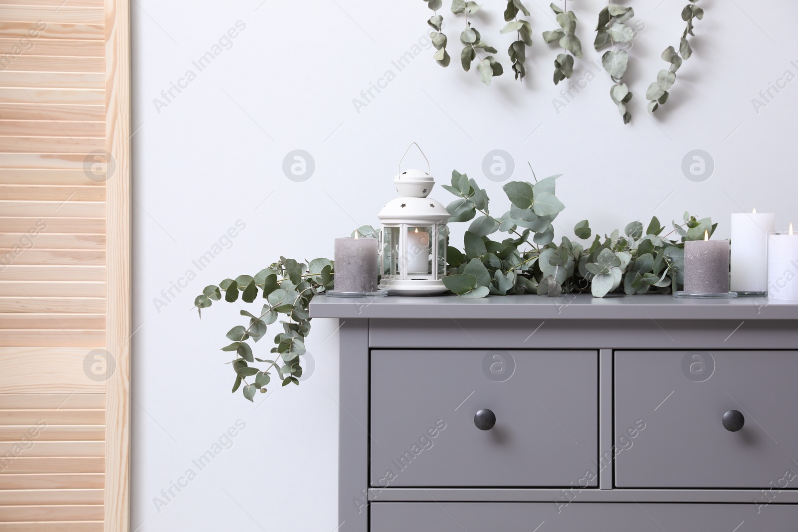 Photo of Stylish chest of drawers decorated with beautiful eucalyptus garland and candles indoors