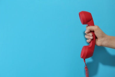 Photo of Closeup view of woman holding red corded telephone handset on light blue background, space for text. Hotline concept
