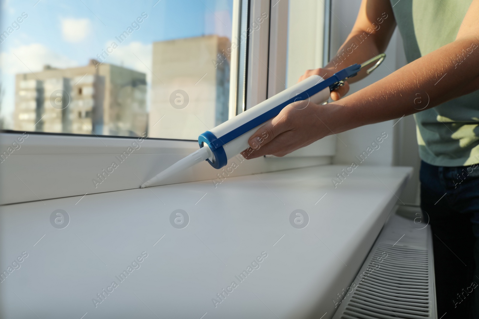 Photo of Construction worker sealing window with caulk indoors, closeup