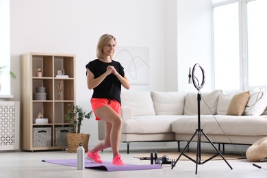Photo of Smiling sports blogger streaming online fitness lesson with smartphone at home