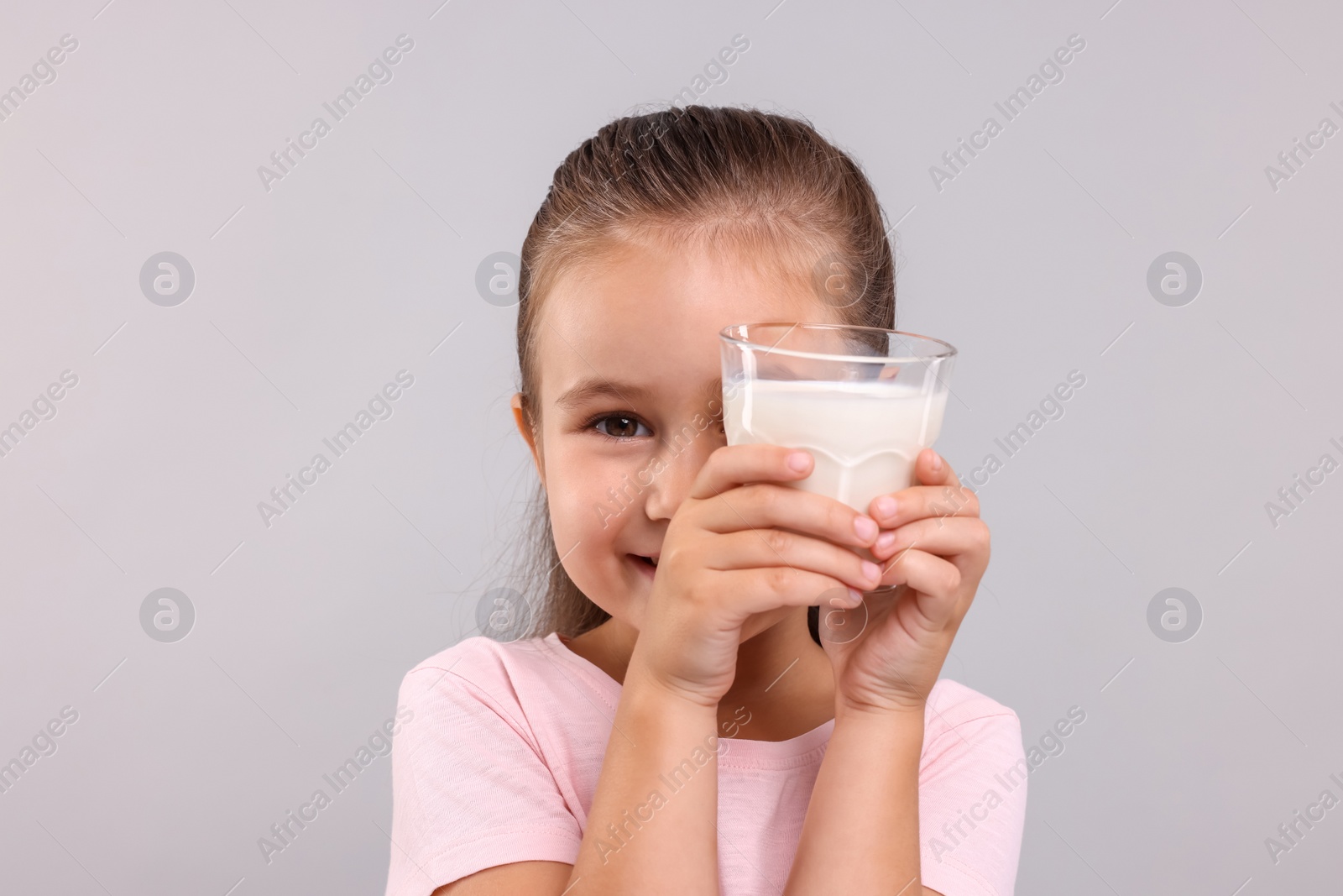 Photo of Cute girl with glass of fresh milk on light grey background