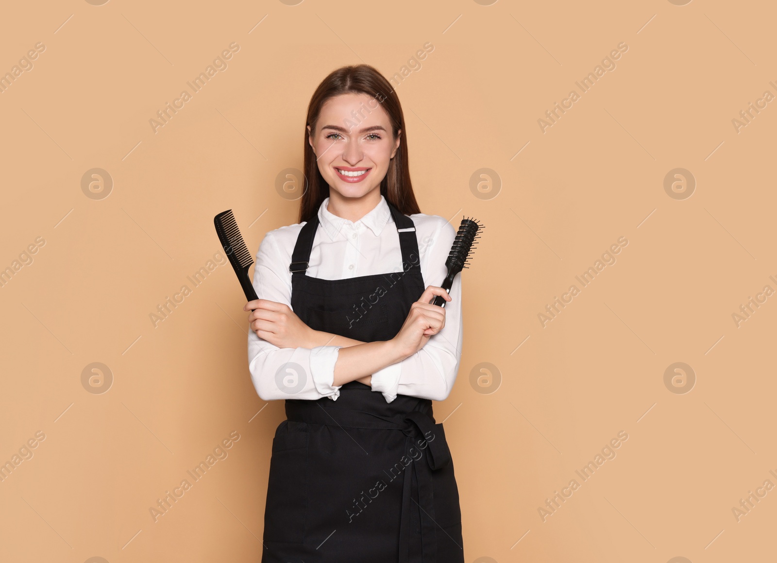 Photo of Portrait of happy hairdresser with brush and comb on beige background. Space for text