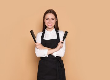 Portrait of happy hairdresser with brush and comb on beige background. Space for text